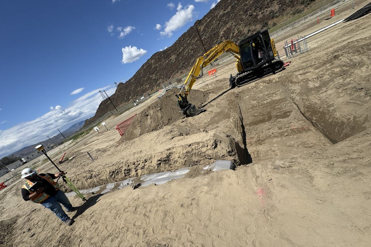 Excavator and crew constructing a drainfield on a sand pad below a rock cliff