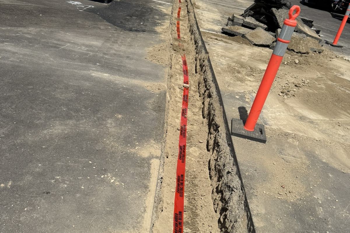 Long conduit trench cut through an asphalt parking lot with cones