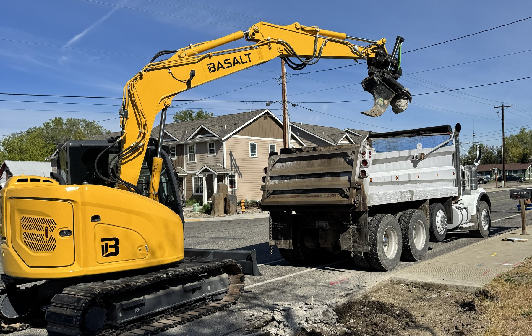 Basalt excavator with tiltrotator loading a dump truck on a residential street