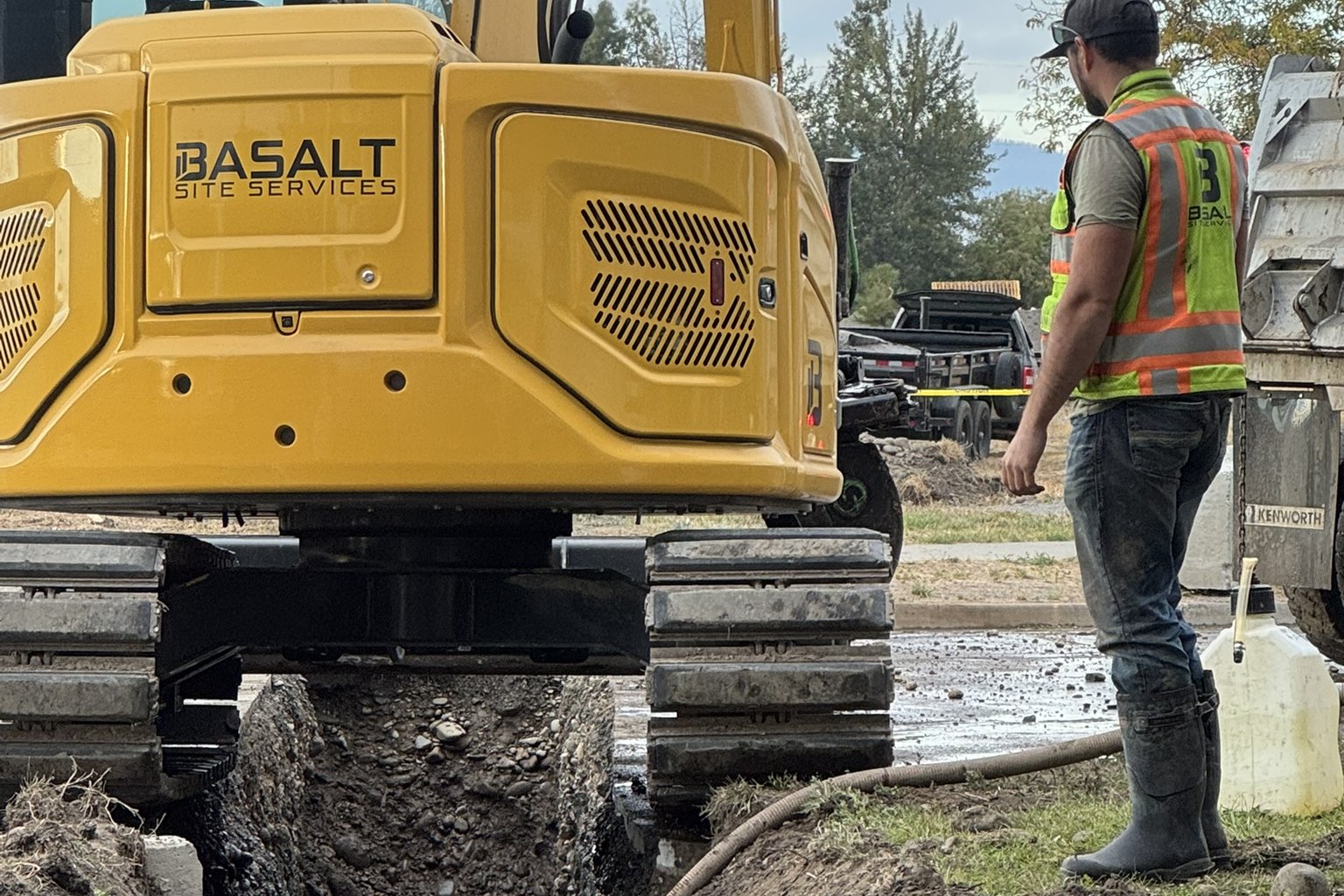 Basalt excavator straddling an open utility trench with a crew member on site