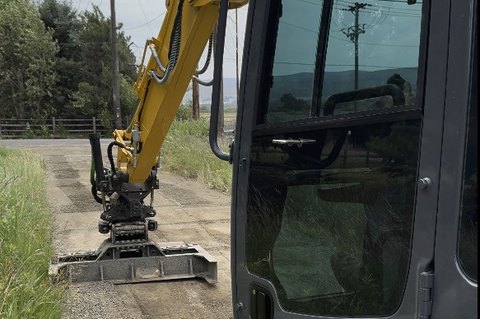 Excavator with a Steelwrist tiltrotator and grading beam trimming a gravel road shoulder